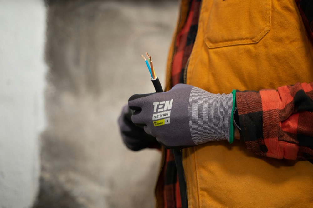 Hand im Arbeitshandschuh hält ein abisoliertes dreiadriges Kabel